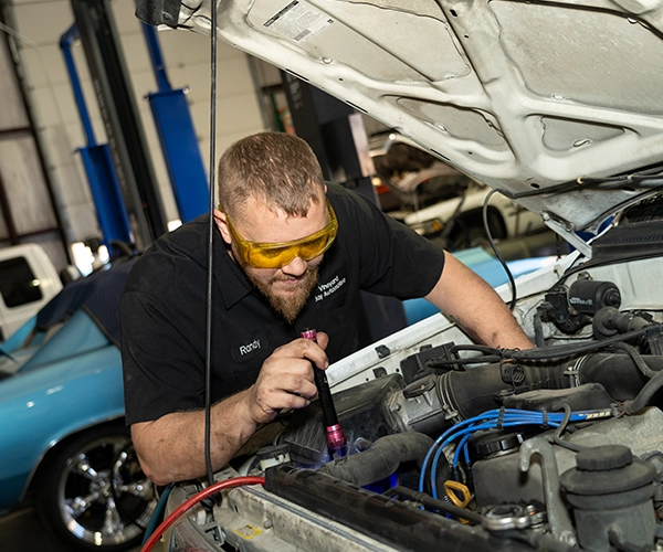 Technician inspecting engine bay with flashlight